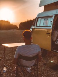 Rear view of man sitting on seat against sky during sunset
