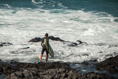 Rear view of man standing on rock in sea