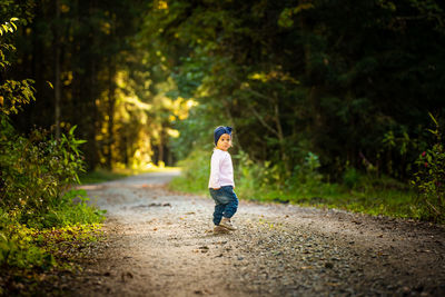 Full length of baby girl standing on dirt road amidst forest