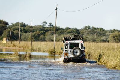 Vintage rough terrain safari car driving through flooded road against clear sky