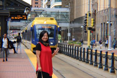 Portrait of mature woman smiling while standing at railroad station platform in city