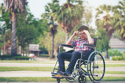 Boy suffering from headache sitting on wheelchair on footpath