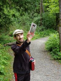 Mid adult man taking selfie with smart phone while standing against plants in forest