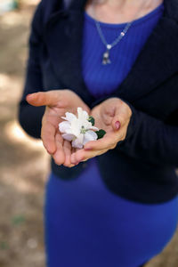 A woman holds an apple tree flower in her palms in spring on a blurred background of a blue dress 