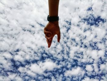 Cropped hand gesturing against cloudy sky