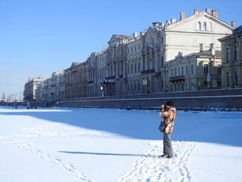 Woman standing by building against sky during winter