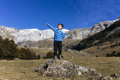 Boy standing on rock against clear blue sky