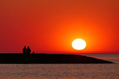 Silhouette people by sea against orange sky during sunset