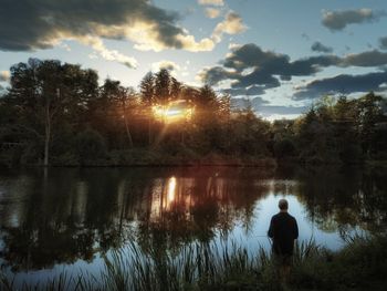 Rear view of silhouette man by lake against sky during sunset