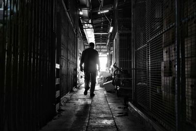 Rear view of man walking on illuminated corridor