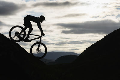 Silhouette cyclist riding on mountain against sky