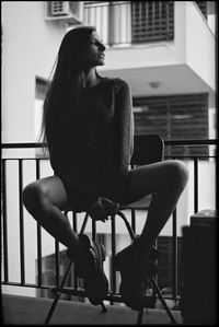 Full length of young woman sitting on chair in balcony