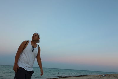 Portrait of young woman standing on beach against clear sky