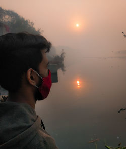 Portrait of man looking at lake against sky during sunset