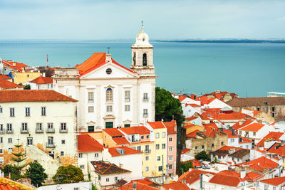 Buildings in town by sea against sky