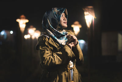 Young woman wearing hijab against illuminated lanterns at night