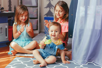 Sisters clapping while looking at brother in playroom