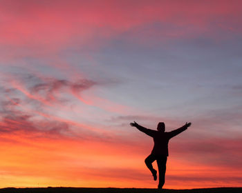 Silhouette man with arms raised standing against sky during sunset