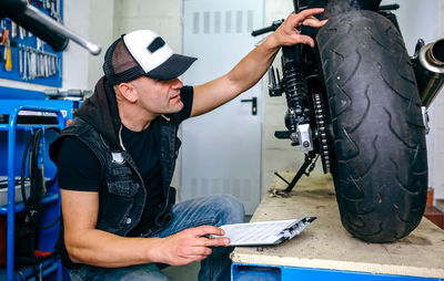 Side view of mature mechanic examining motorcycle in garage