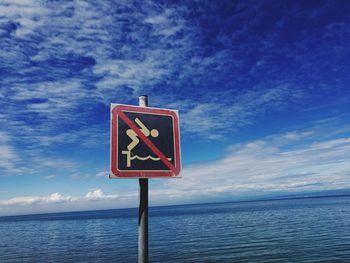 Information sign by sea against blue sky