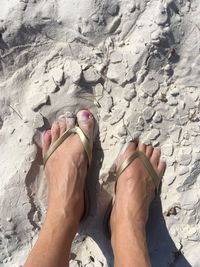 Low section of woman wearing flip-flop while standing in sand at beach