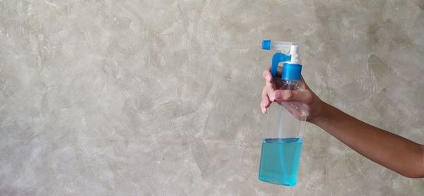 Midsection of person holding bottle against wall