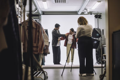 Male design professional assisting fashion model during photo shoot in studio