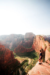 Rear view of man standing at cliff looking at landscape