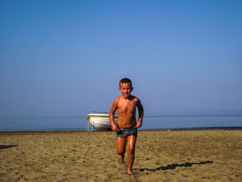 Full length of shirtless man standing at beach against clear sky