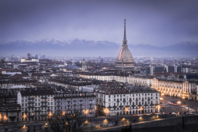 Illuminated buildings in city against cloudy sky