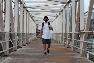 Young millennial walking on footbridge while wearing a protective mask to prevent covid-19 infection
