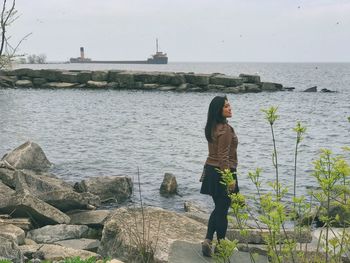 Full length of woman standing on rock by sea against sky