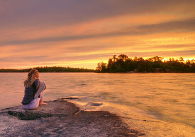 Woman sitting on land against sky during sunset