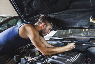 Side view of dirty man loosening screws on motor while fixing car in garage