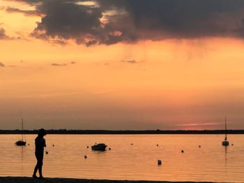 Silhouette woman standing on sea against sky during sunset