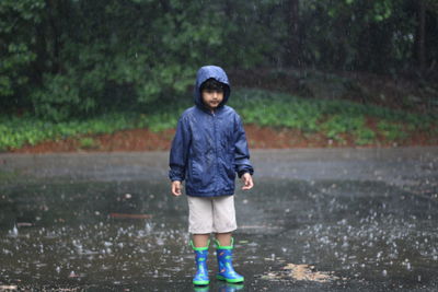 Portrait of boy wearing raincoat standing amidst road during rainy day