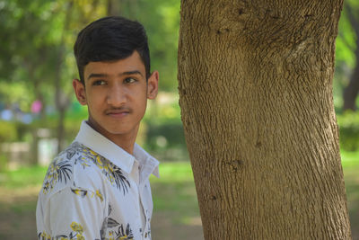 Portrait of young man standing by tree trunk
