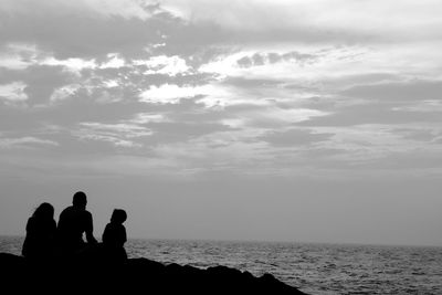 Silhouette people sitting at beach against sky
