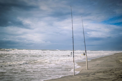 Fishing rods on shore at beach against cloudy sky