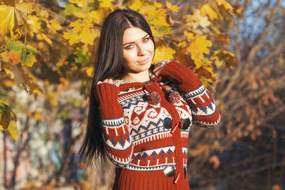 Young woman looking away while standing against trees during autumn