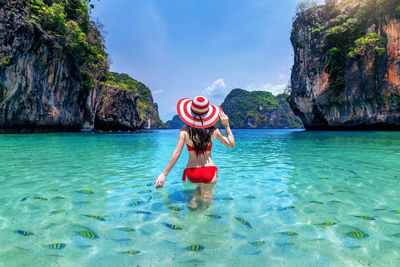 Rear view of woman jumping in sea against sky