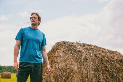 Man standing by hay bale on field against sky