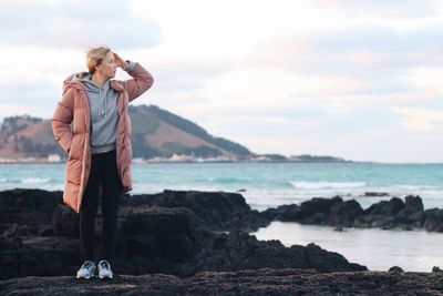 Full length of woman standing on rock by sea against sky