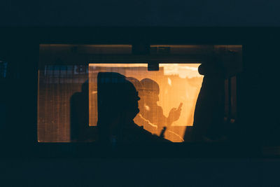 Silhouette people in train seen through window during sunset