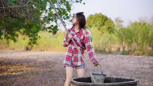 Young woman putting pole in well at farm