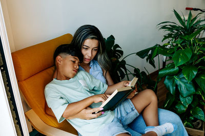 Young family mother and son reading a book in sofa at home