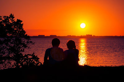 Silhouette couple standing by sea against orange sky during sunset