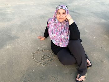 Portrait of smiling mid adult woman sitting by heart shape on sandy beach