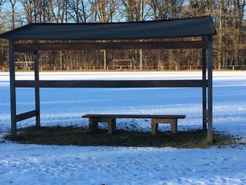 Empty bench by trees against sky