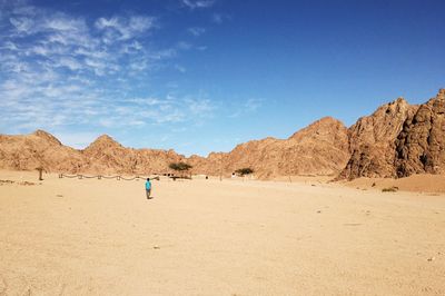 Man standing on sand dune in desert against blue sky
